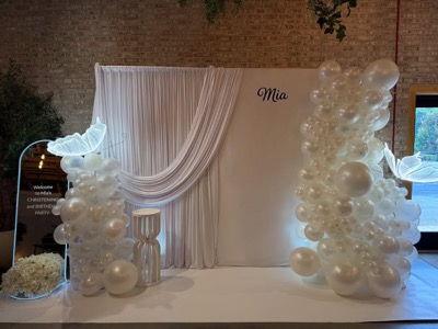 White drape backdrop with pearl balloon columns and lit butterflies